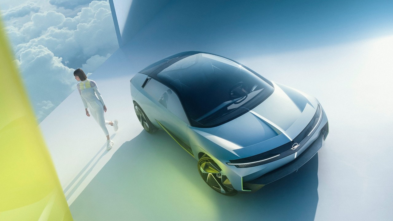 Bovenaanzicht voorkant van een zilveren Opel Experimental met een vrouw die ernaast loopt.