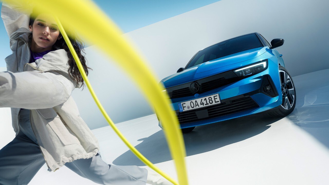 Front view of a blue Opel Astra Electric with woman twirling a yellow charging cable